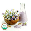 Wild Aster flowers in a wooden bowl, glass flask with powder, and USDA Organic label on a white background
