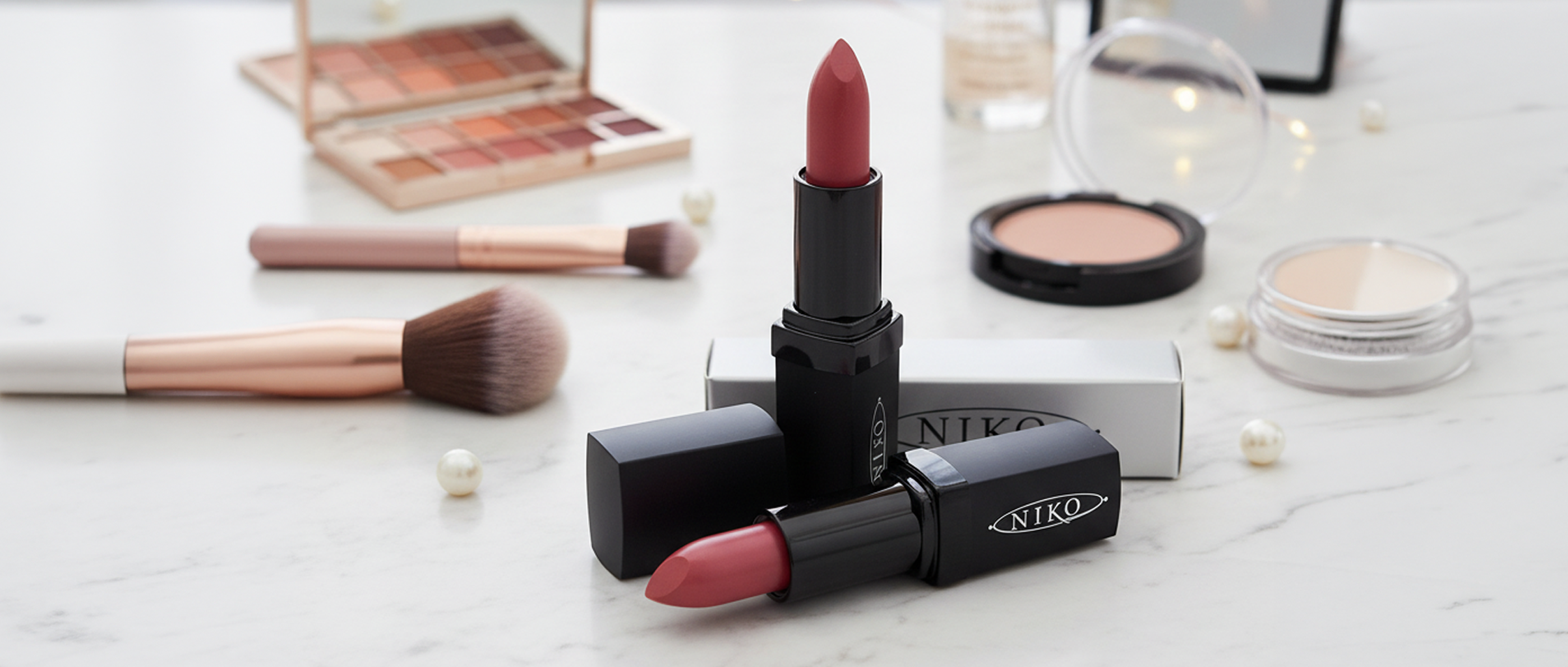 Nikko lipstick with makeup brushes and palette on a light surface