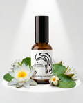An amber glass bottle with a black cap and a white label reading 'Muskoka Wild Harvest', styled with white water lilies and green lily pads on a white surface against a white background with soft spotlighting.